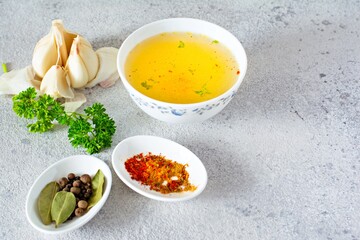 Homemade chicken (bone) broth/bouillon with vegetables, spices and herbs in a bowl (cup) on a light background. Natural collagen of animal origin. Liquid broth from meat, fish, vegetables.