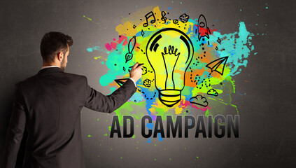 businessman drawing colorful light bulb with AD CAMPAIGN inscription on textured concrete wall, new business idea concept