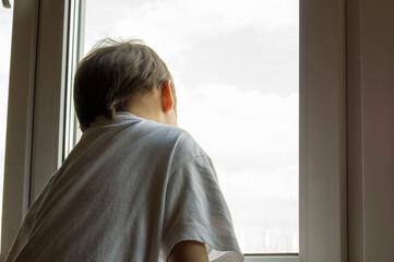 A little boy looks out the window. The street is bright and sunny. Cold weather