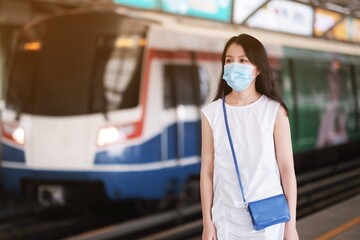 Asian girl wear surgical mask to protect the Covid-19 virus in sky train station, New normal lifestyle