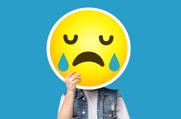 Unrecognizable man hiding his face behind crying sad emoticon emoji