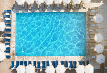 Lounge chairs with umbrellas near swimming pool on sunny day, top view