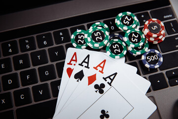 Online casino concept. Gambling chips and playing cards on laptop keyboard.