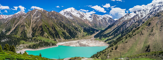Panoramic view of the mountain lake opposite the snow-capped mountain range.