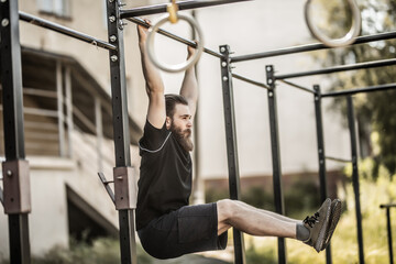 Pull-up strength training exercise. Fitness man working out his arm muscles on outdoor beach gym doing chin-ups pull-ups as part of a crossfit workout routine.