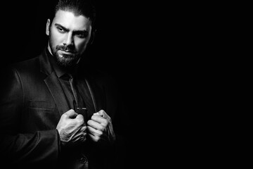 Business portrait of a white caucasian man in a black classic suit on a black background. Bearded...