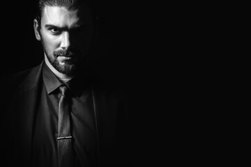 Portrait of a white Caucasian male brunet in a black classic suit, black shirt and black tie over a black background. Fashionable portrait of an attractive man with dark hair. - Powered by Adobe
