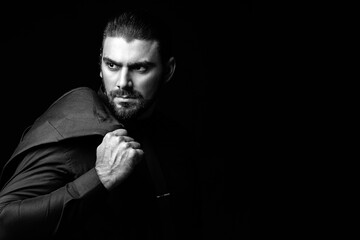 Portrait of a white Caucasian male brunet in a black classic suit, black shirt and black tie over a black background. Fashionable portrait of an attractive man with dark hair.