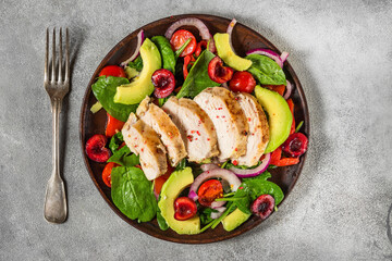 Salad with grilled chicken breast, avocado, spinach, cherry berries and tomato in a plate with fork. top view