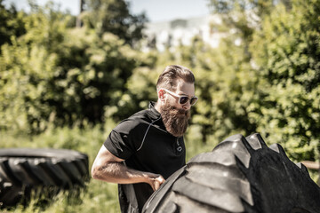 Full length side view of young man athlete flipping large tire outside gym