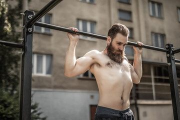 Fitness, sport, exercising, training and lifestyle concept. Young man doing pull ups on horizontal bar outdoors