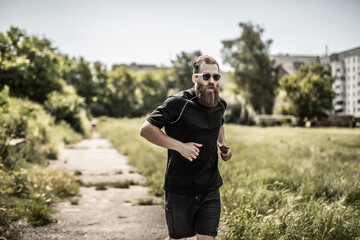 Young happy cheerful smiling bearded man, during morning jogging outdoors. Fitness, sport, exercising, crossfit and workout concept.