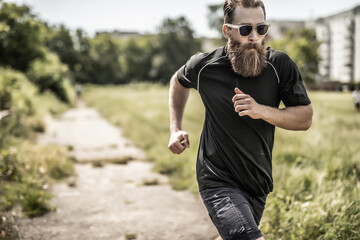 Fototapeta premium Young happy cheerful smiling bearded man, during morning jogging outdoors. Fitness, sport, exercising, crossfit and workout concept.