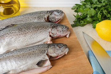 Close-up of three raw gutted trout fishes on a wood cutting board prepared for cooking. Fresh fish dishes, healthy eating and cook at home concept.