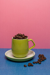 Lime green coffee cup and saucer filled with fresh coffee beans with colourful pink and blue background 