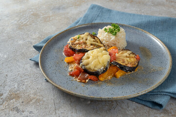 Eggplant, tomato and bell pepper baked with cheese and rice on a blue plate and a rustic gray background, copy space, selected focus, narrow depth of field