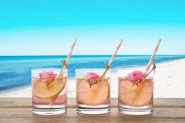 Tasty refreshing drink on wooden table against sandy beach