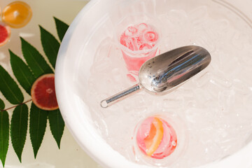 Large bathroom with ice cubes, fruits grapefruit, orange, lemon, green leaves and cocktails. Welcome zone of drinks with colourful lemonades. Non-alcoholic healthy drinks.