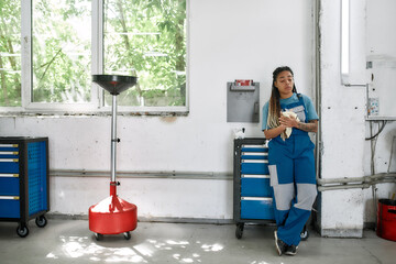 The essence of true service. Young african american woman, professional female mechanic looking down, wiping, cleaning her hands with cloth after repairing a car in auto repair shop