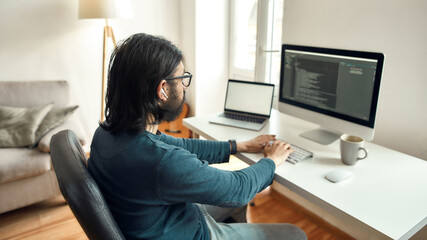 Software Programming. Side view of young male web developer wearing eyeglasses writing code on...