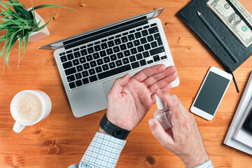 Businessman disinfecting hands while working office desk