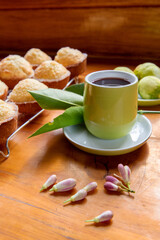 A full green cup and saucer filled with tea and garnished with a lemon leaf with freshly baked lemon muffins in the background 
