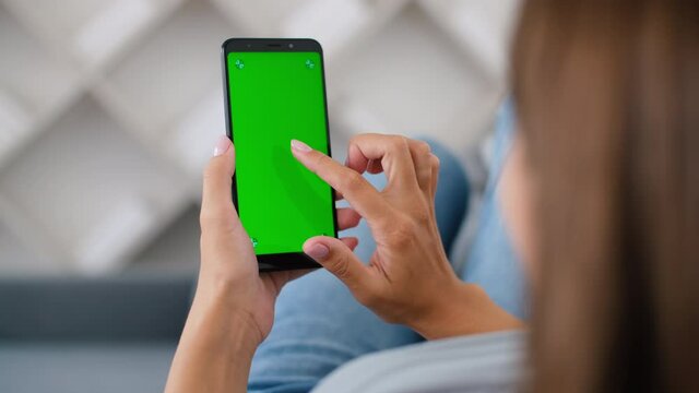Rear view of woman in modern room sitting on couch using phone with green screen mockup Chroma Key with trackpoints surfing internet Viewing content Video Blogging. One click 4K