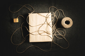 Close up of string looped over a brown paper package leading to a child's block with a question mark on a textured grey background.