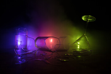 Broken glasses on wooden table at dark toned background with fog. Selective focus