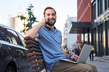 Merry man with notebook talking on smartphone outdoors