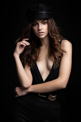 Fashionable studio portrait of a beautiful young model in black hat and sexy top on a black background. Low key.