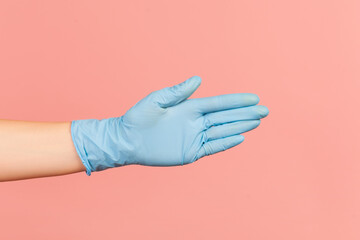 Profile side view closeup of human hand in blue surgical gloves giving hand to greeting or touching. indoor, studio shot, isolated on pink background.