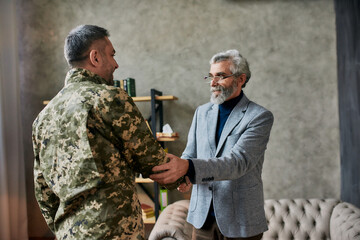 Real help. Mature psychologist smiling, shaking hands with middle aged military man after therapy...