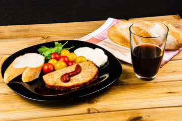 Classic meatloaf, cherry tomatoes, mozzarella, parsley, white bread in a black plate on a wooden background. Glass of pomegranate juice
