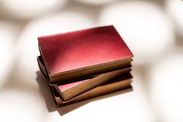 Stack of three old books with crimson covers on an isolated white background with patterned lighting