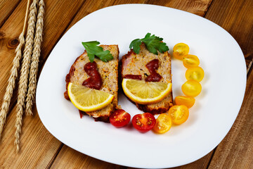 Classic meatloaf, cherry tomatoes, lemon wedge, parsley in a white plate on a wooden background. Ears of wheat