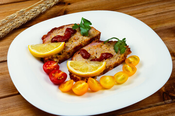 Classic meatloaf, cherry tomatoes, lemon wedge, parsley in a white plate on a wooden background. Ears of wheat