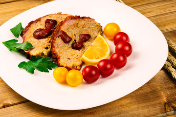 Classic meatloaf, cherry tomatoes, lemon wedge, parsley in a white plate on a wooden background. Ears of wheat