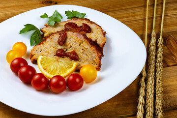Classic meatloaf, cherry tomatoes, lemon wedge, parsley in a white plate on a wooden background. Ears of wheat