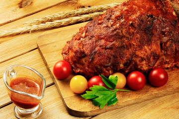 Classic meatloaf on a cutting board on a wooden background. In the background are red and yellow cherry tomatoes, parsley, ears of wheat
