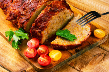 Classic meatloaf on a cutting board on a wooden background. In the background are red and yellow cherry tomatoes, parsley, ears of wheat