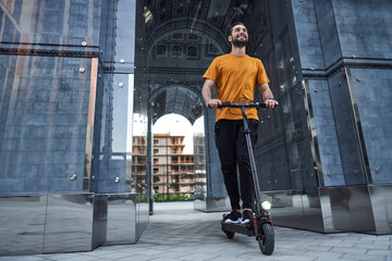 Cheerful young man using scooter in city