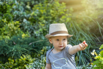 Cute little baby boy  with a hat on his head is showing strawberry in the garden.