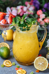 Summer fresh cold drink beverages. Ice Lemonade in the jug and lemons and orange with mint on the table outdoor. Orange lemonade in a jug