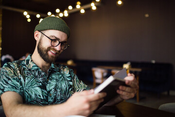 Happy smiling smart bearded hipster man reading book in cafe and smiling