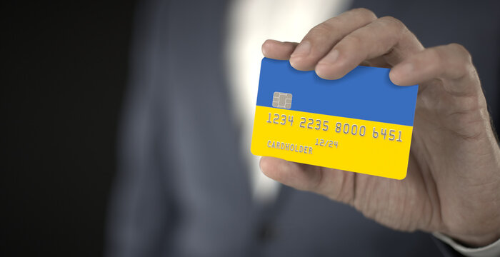 Businessman holding plastic bank card with printed flag of Ukraine in his hands, fictional numbers