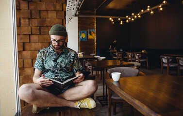 Modern hipster guy reading book in cafe