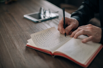 A young man writes in a notebook at the table. Hands with pen and notepad close-up