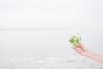 The hand of a young girl holds out a cocktail. Summer fruit drink in a glass. relaxation, party and...