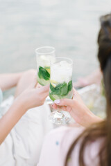 Girls holding fresh lemonade in glass. Healthy vegan lifestyle. Lemons, oranges with mint in the glass.